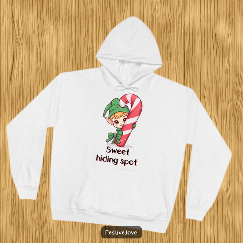 Funny hoodie design of a cheeky elf character peeking slyly from behind a giant, striped candy cane.